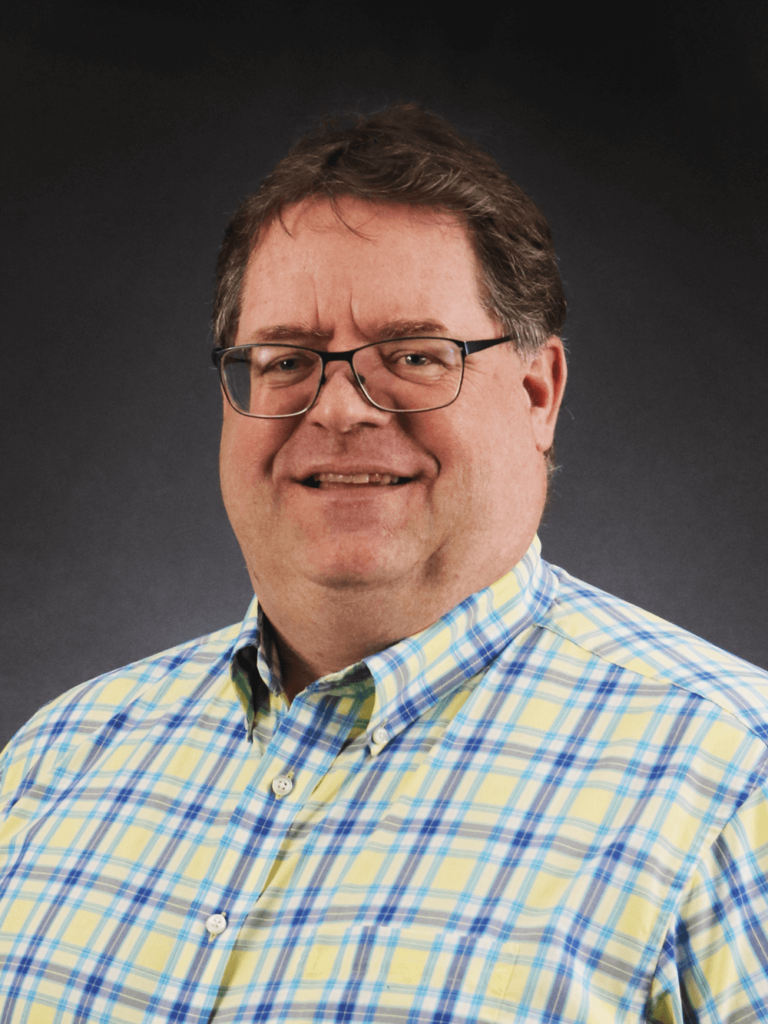 Jeff Kubsch Headshot Jeff Kubsch smiling for a headshot from the chest up while wearing a yellow and blue short-sleeve checkered shirt and glasses