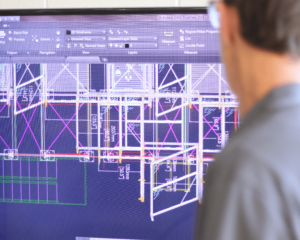 A male engineer is viewing a wireframe of a custom fencing project on a large monitor